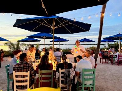 a group of people sitting at a beach umbrella eating and appreciating a florida keys sunset